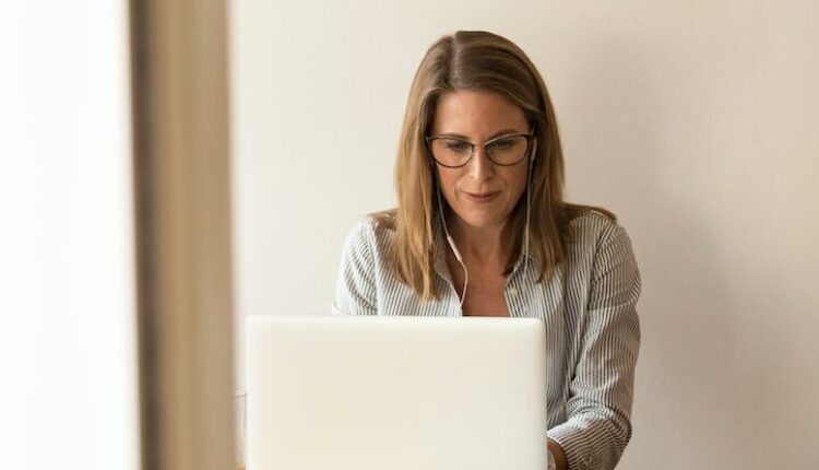 woman wearing grey striped dress shirt sitting down near brown wooden table in front of white laptop computer